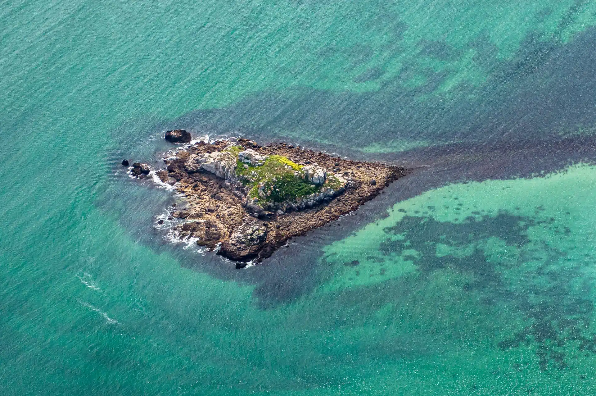 Petite île rocheuse entourée d'eau turquoise brillante.