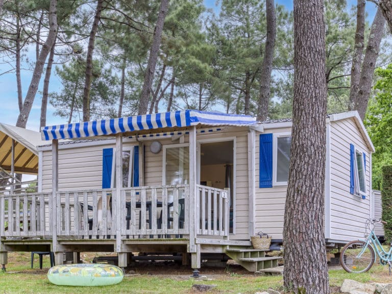 Mobil-home en forêt avec terrasse et vélo.
