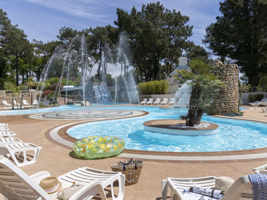 Piscine extérieure avec jets d'eau, transats autour.