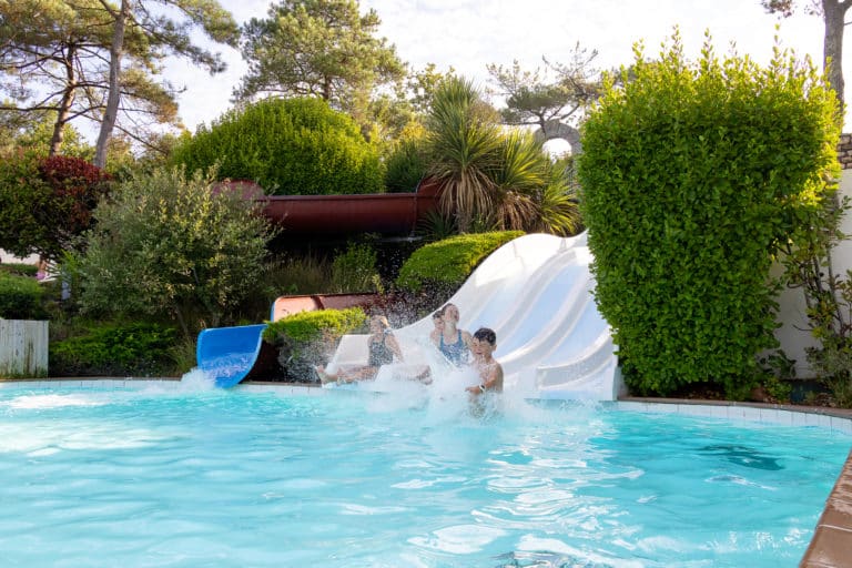 Personnes glissant sur toboggan aquatique dans piscine extérieure.